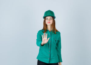 young lady in shirt, pants, helmet showing stop gesture and looking serious , front view.
